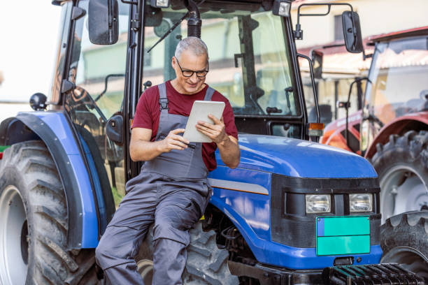 man using digital tablet and sitting on a tractor - photography gray hair farmer professional occupation imagens e fotografias de stock