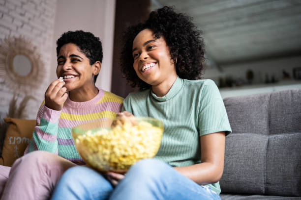 amici che guardano la tv e mangiano popcorn a casa - alternative health care foto e immagini stock