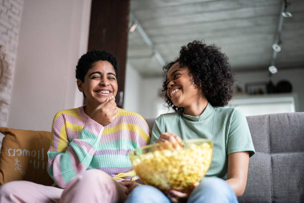 des amis qui regardent la télévision et mangent du maïs soufflé à la maison - healthy lifestyle people eating sister photos et images de collection