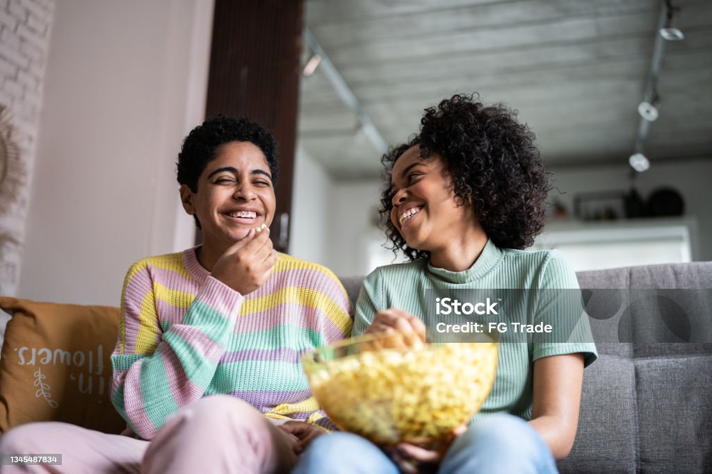 Friends watching TV and eating popcorn at home Television Set Stock Photo