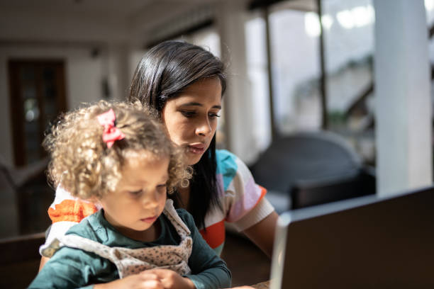 istock Mother using a laptop while holding her daughter at home 1345489128