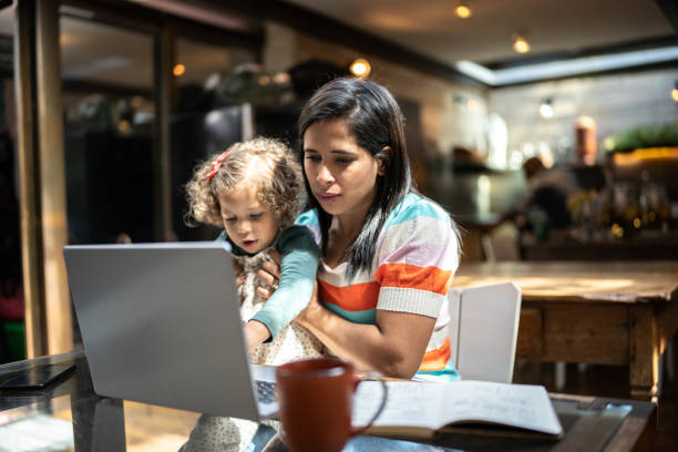 istock Mother using a laptop while holding her daughter at home 1345489146
