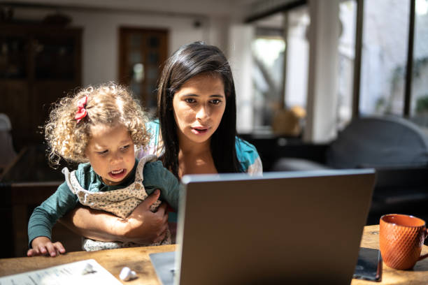 istock Mother using a laptop while holding her daughter at home 1345489151