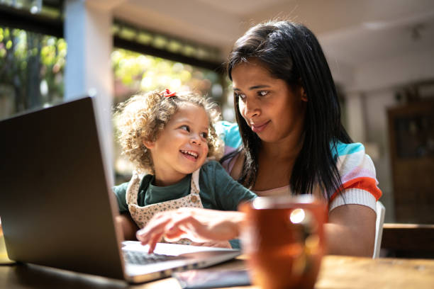 istock Mother using a laptop while holding her daughter at home 1345489154