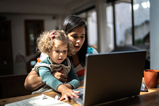 istock Mother using a laptop while holding her daughter at home 1345489188