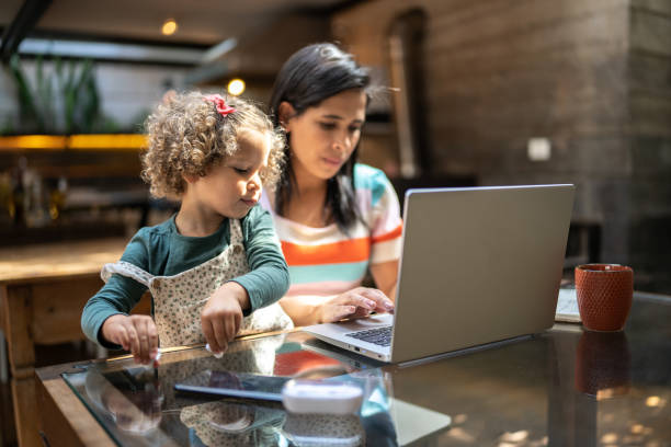 istock Mother using a laptop while holding her daughter at home 1345489277