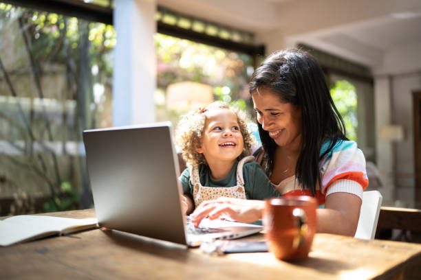 istock Mother using a laptop while holding her daughter at home 1345489323