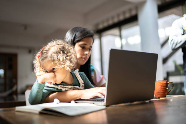 istock Mother using a laptop while holding her daughter at home 1345489325