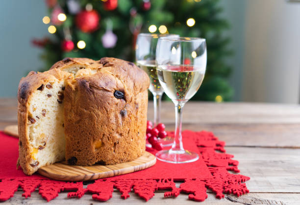 panettone e bicchieri da vino su tavolo in legno con decorazioni natalizie e albero sullo sfondo. - fruitcake christmas cake cake raisin foto e immagini stock