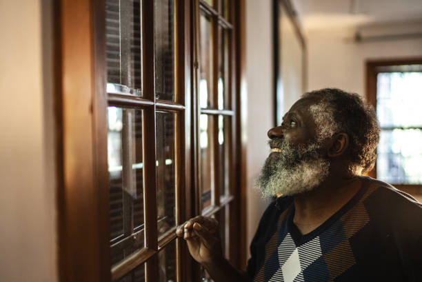 istock Senior man looking through the window at home 1345489446