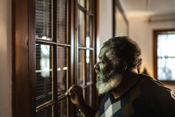 hombre mayor mirando por la ventana de casa - pensive senior adult looking through window indoors fotografías e imágenes de stock