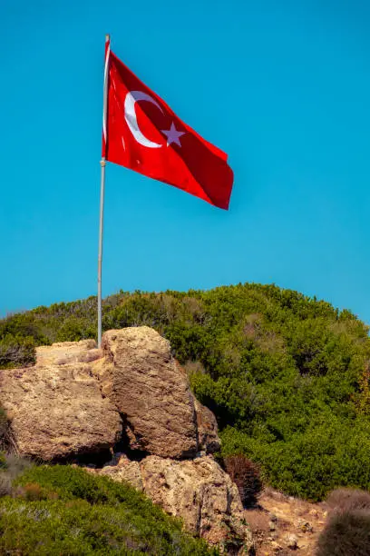 The Turkey National flag waiving on the rocky hill of an island against a blue sky