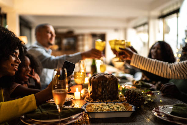 Young woman doing a video call/filming/taking photos of the family toasting on Christmas dinner at home Young woman doing a video call/filming/taking photos of the family toasting on Christmas dinner at home family christmas party stock pictures, royalty-free photos & images