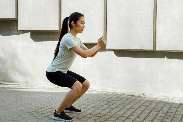 istock Asian sportswoman does squats at training near stone steps 1345499298