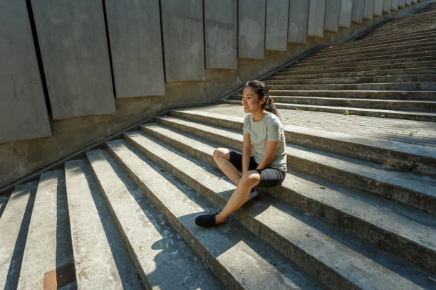 istock Asian woman in tracksuit sits resting on empty grey steps 1345503949
