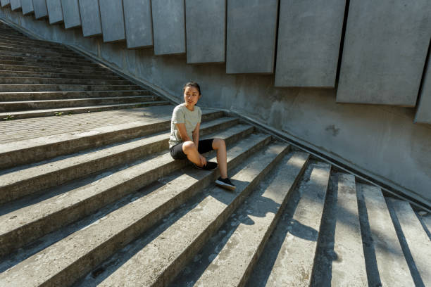 istock Asian woman in tracksuit sits resting on empty grey steps 1345504164