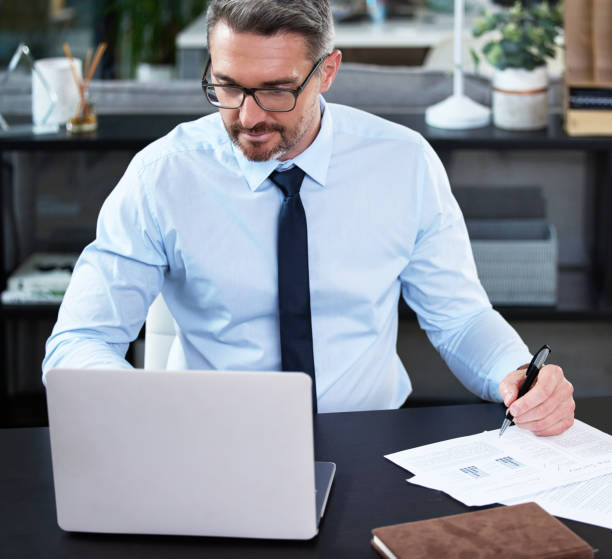 istock Shot of a mature businessman using a laptop while going through paperwork in an office at work 1345504204