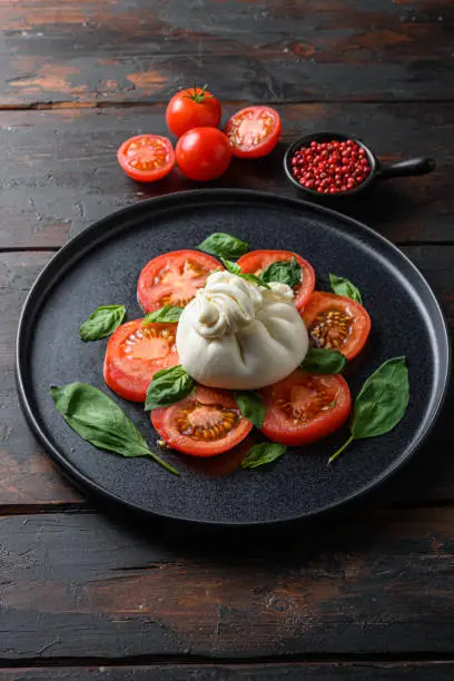 Burrata, Italian fresh cheese made from cream and milk of buffalo or cow.  on black plate old wood table planks.