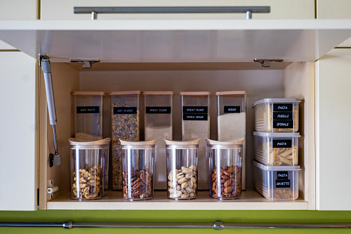 Domestic healthy vegetarian dry food storage organization on shelf at kitchen cupboard. Comfortable neatly keeping arrangement in glass containers oat flakes, wheat flour, sugar, pasta, nuts, rice