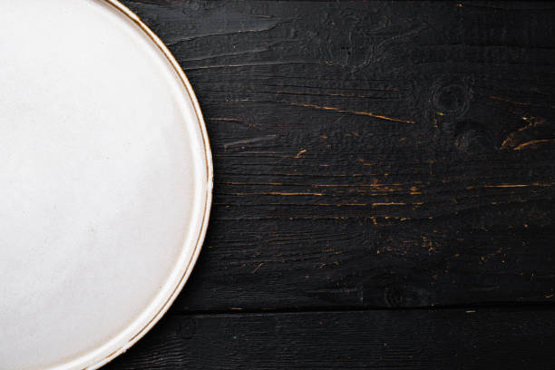 istock White rustic ceramic plate with copy space for text or food with copy space for text or food, top view flat lay , on black wooden table background 1345507782