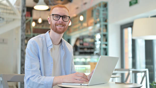 istock Redhead Man with Laptop Smiling at Camera in Cafe 1345508605