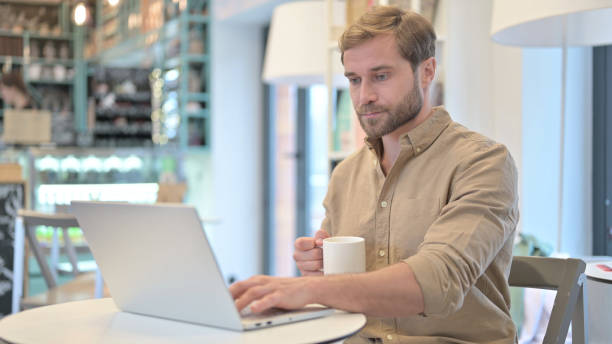 man holding coffee cup while working on laptop - 24187 imagens e fotografias de stock