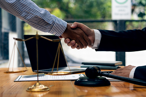 On a table with scales and hammers placed in front of the businessman shakes hands, making a deal with a lawyer. male judge legal counsel Contract consulting services to plan a lawsuit in court
