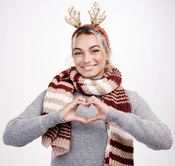 Studio portrait of an attractive young woman making a heart shape with her hands while dressed in Christmas-themed attire