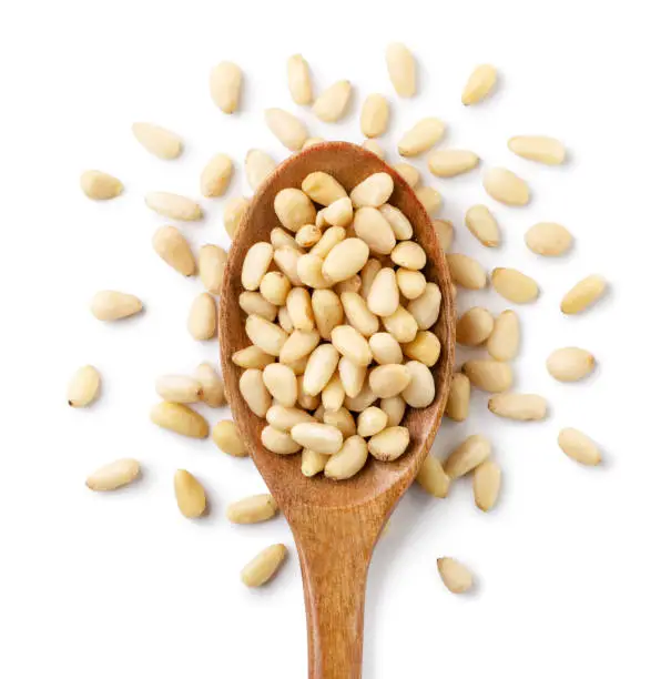 Pine nut in a wooden spoon and scattered close-up on a white background. Top view