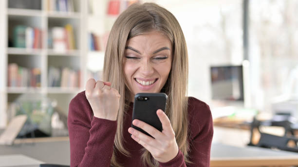 istock Young Woman Celebrating Success on Smartphone 1345514807