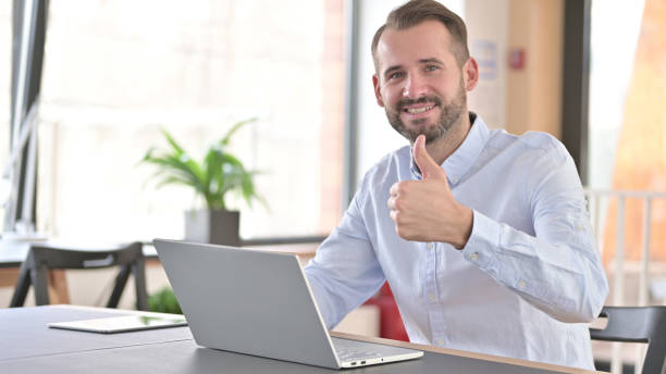 istock Young Man with Laptop doing Thumbs Up in Office 1345515560