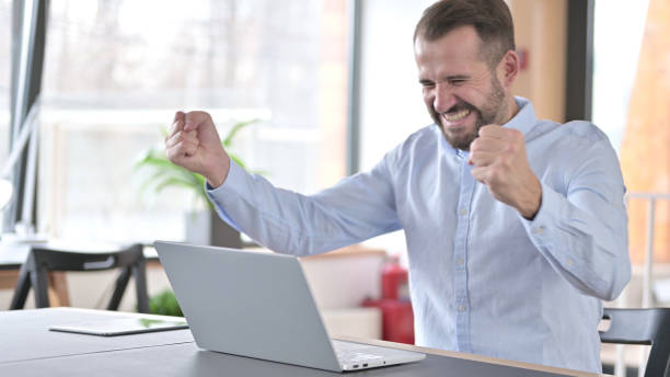 istock Young Man Celebrating Success on Laptop in Office 1345516498