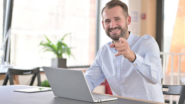 istock Cheerful Young Man with Laptop Pointing with Finger 1345516920