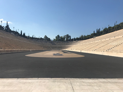 Athens, Greece - Jul 13, 2019: The main field of Panathenaic Stadium in Athens, famous tourist attraction - hosted the first modern Olympic Games in 1896 and it is the only stadium in the world built entirely of marble. Taken on mobile device.Athens, Greece - Jul 13, 2019: Symmetrical view of empty Panathenaic Stadium from the audience on sunny day. Panathenaic Stadium called Kallimarmaro in Athens. Taken on mobile device.