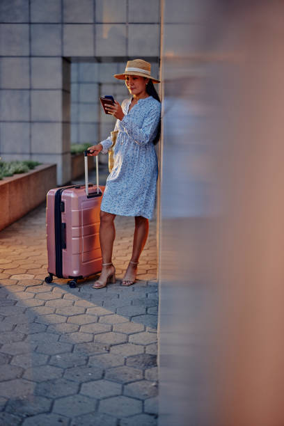 istock One beautiful asian woman with her suitcase while checking her schedule with her phone. 1345518196