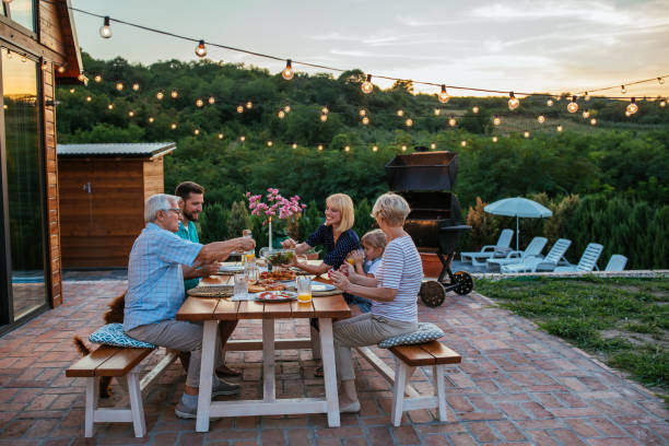 Multi-generations family gathering at dinner party in the backyard Happy family eating together outdoors. Smiling generation family sitting at dining table during dinner. Happy cheerful family enjoying meal together in garden. dinner party photos stock pictures, royalty-free photos & images