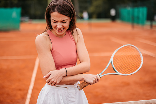 Woman holding elbow in pain while playing tennis