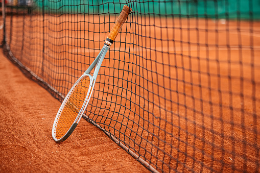 Tennis racket leaning on net on clay court.