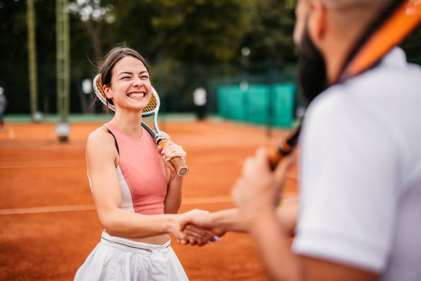 Tennis players shaking hands over tennis net Two young tennis players, male and female, shaking hands together outdoors on the court over tennis net. Sportsmanship and Respect: stock pictures, royalty-free photos & images