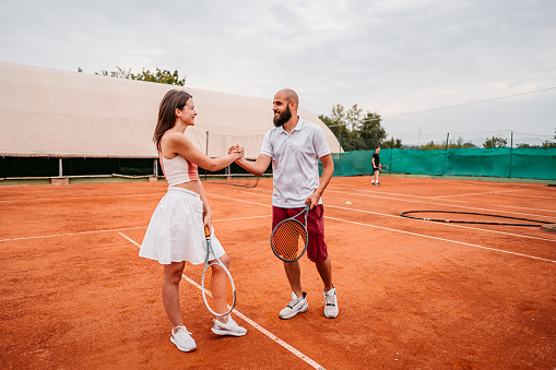 Two young tennis players, male and female,  shaking hands together outdoors on the court.