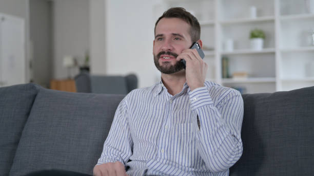 istock Cheerful Young Man Talking on Smart Phone at Home 1345522806