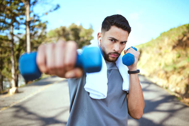 portrait of a sporty young man doing dumbbell punches while exercising outdoors - healthy lifestyle men boxing dumbbell imagens e fotografias de stock