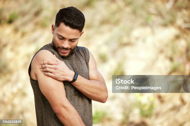 Shot Of A Sporty Young Man Holding His Shoulder In Pain While Exercising Outdoors Stock Photo - Download Image Now