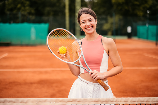 Portrait of active smiling young woman on the tennis court with tennis racket in hand.