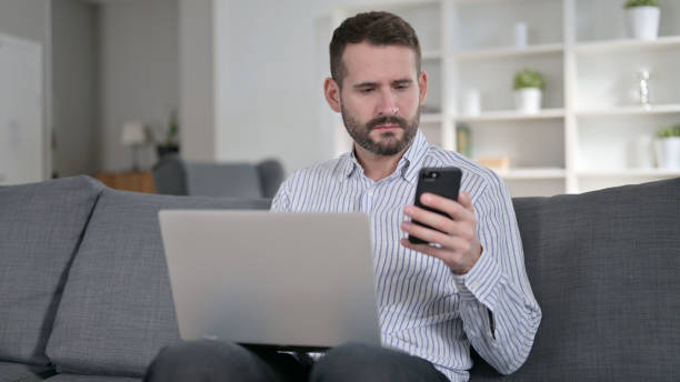 istock Focused Man working on Smartphone and Laptop at Home 1345523176