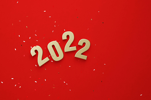 Gold colored 2022 sitting beneath falling confetti over red background. 2022 ne year concept. Horizontal composition copy space. Directly above.