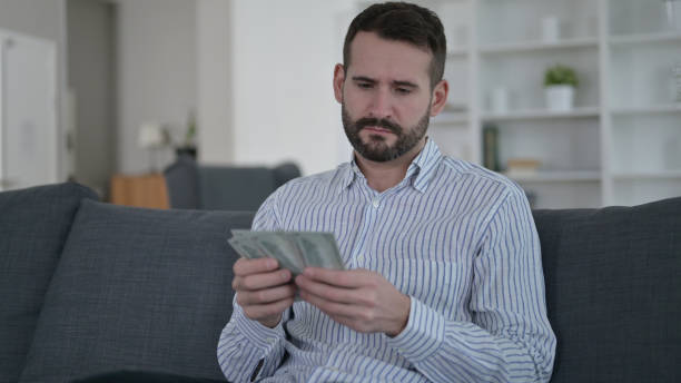 istock Worried Young Man Counting Dollars at Home 1345523232