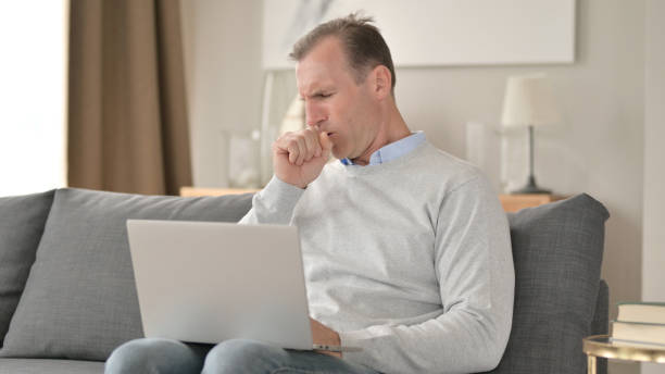 istock Sick Middle Aged Businessman Coughing on Sofa 1345524804