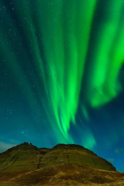 Photo of Northern lights in Iceland. Landscape full of kp5 Aurora Borealis. Amazing nightscape at Kirkjufell, scenic travel destination. Green sky full of stars.