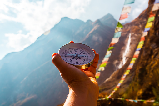 Round compass in hand on the background of blurred mountain and prayer buddhist flags fluttering in the wind. Concept for travelling and active lifestyle. Nepal, Himalaya